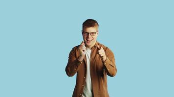 Young smiling caucasian man pointing with fingers to the camera with both hands on a blue background in the studio. Concept of win and success video