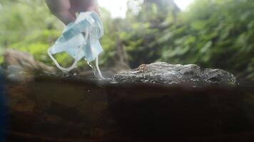 eco voluntario a mano tomando usado médico máscara fuera desde bosque arroyo en submarino ver cerca arriba. cuidando persona pensando acerca de futuro y voluntariamente peleas en contra ambiental contaminación. video