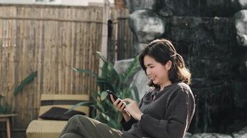 Smiling Asian woman using smartphone at cafe while looking at her online social media. Relax time video