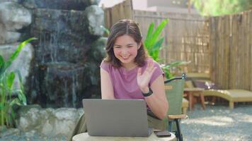 Online meeting via internet. Friendly Asian woman greeting making call with laptop in cafe, waving hand at camera. work from anywhere concept video