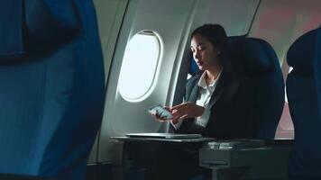 exitoso asiático negocio mujer, negocio mujer trabajando en avión cabina durante vuelo en ordenador portátil computadora video