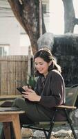 Smiling Asian woman using smartphone at cafe while looking at her online social media. Relax time video