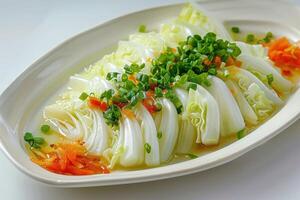 Boiled cabbage, adorned with chopped green onion, a small amount of sweet pepper, light soy sauce, oval shaped white plate. photo