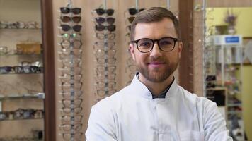 Attractive young doctor in ophthalmology clinic. Doctor ophthalmologist is standing near shelves with different eyeglasses video