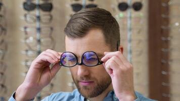 A funny man puts glasses incorrectly. A man is having fun in optics when choosing glasses video