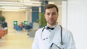 Smiling young Caucasian male doctor in white medical uniform show good quality service in hospital. Headshot portrait of happy man GP or pediatrician in clinic. Healthcare concept video