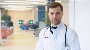 Male doctor invites for treatment in a modern clinic. Headshot portrait of happy man GP or pediatrician in clinic video