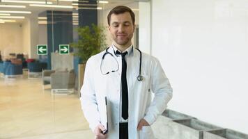 Smiling young Caucasian male doctor in white medical uniform show good quality service in hospital. Headshot portrait of happy man GP or pediatrician in clinic. Healthcare concept video