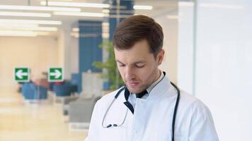 Male doctor invites for treatment in a modern clinic. Headshot portrait of happy man GP or pediatrician in clinic video