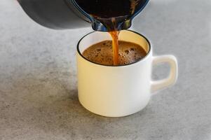 Pouring coffee from cezve in cup on white background photo