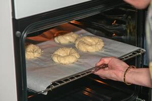a woman puts a baking sheet with homemade sesame buns in the oven 3 photo