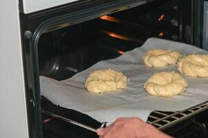 a woman puts a baking sheet with homemade sesame buns in the oven 2 photo