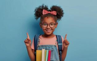 Happy Young Girl With Backpack Pointing Up Against A Blue Background photo