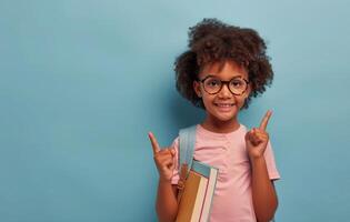 Happy Young Girl With Backpack Pointing Up Against A Blue Background photo