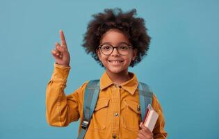 Happy Young Girl With Backpack Pointing Up Against A Blue Background photo