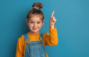 Happy Young Girl With Pigtails Points Up In Front Of Blue Background photo