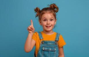 Happy Young Girl With Pigtails Points Up In Front Of Blue Background photo