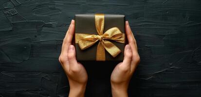 Close Up Of Hands Holding Gold Gift Box With Bow photo