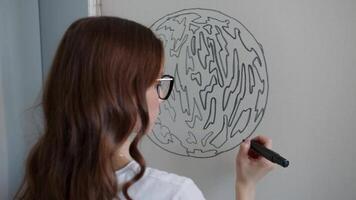 Jeune artiste soigneusement dessine le grandes lignes de une planète, avec ses continents et îles, sur une pièce de en tissu en utilisant une marqueur. cette volonté servir comme une modèle pour création une Douane tapis en utilisant le touffetage technique. video