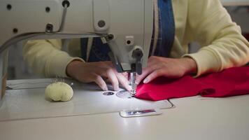 fermer coup de une de couturière mains à travail sur une blanc couture machine, piqûre une pièce de rouge tissu. lent mouvement. 4k video