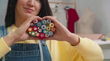 Seamstress carefully folds coils of multicolored thread into a heart shape. She enjoys her work and hobbies, and smiles for the camera. Close up. Slow motion. 4k video