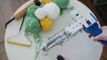 On the table, there are tools for making carpets - balls of colored yarn and a trimmer. A craftswoman picks up a tufting gun from the table. Close up. Slow motion. 4k. video