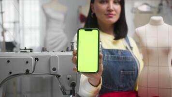 Seamstress, surrounded by sewing tools in her studio, shows the camera the screen of her phone at arm's length, advertising for various applications and websites. Close up. Slow motion. video