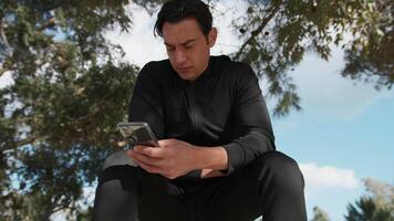 Seated Man In The Park Using Smartphone Under The Trees video