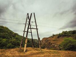 old wooden power pole with concrete support on a hill photo