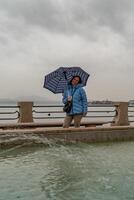Attractive middle-aged woman standing in the rain in front of a fountain on the lakeside promenade photo