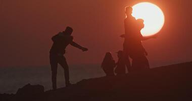 silhouette di persone a tramonto vicino il mare. stile di vita felicità sole raggi Giochi vicino il oceano. alto qualità 4k metraggio video