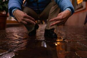 man in blue sneakers bending over a puddle showing the victory sign with his hands on a city street photo