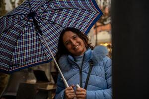 beautiful middle aged smiling woman walking in the rain with an umbrella in front of the tables of an cafe photo