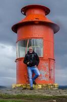 middle aged man photographer posing with camera in front of a red lighthouse photo