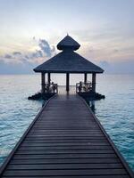 Pier of Maldivian resort at sunrise or sunset, vertical photo