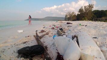 Zoom in time lapse sunny sandy beach with waste plastic bottles and rubbish in famous asia island - tourist destination. Woman people swim in polluted beach after storm video