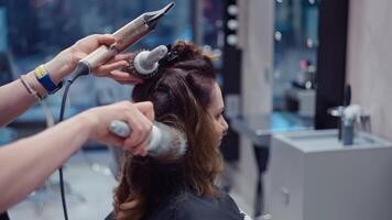 professioneel haar- stileren. deskundige stilist creëert verbijsterend kijken voor vrouw in salon gebruik makend van kam en haardroger, mooi kapsel en kapsel gedaan door professioneel, haar- zorg en Gezondheid. video