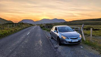 Car driving on empty scenic road trough nature and mountains at sunset, Connemara national park, county Galway, Ireland photo