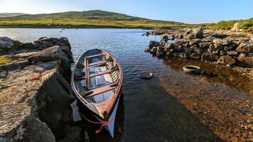 Old wooden fishing boat in lake by Fisherman's hut with mountains in background at Connemara, Galway, Ireland photo