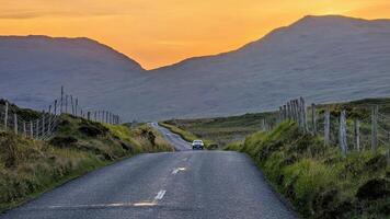 Car driving on empty scenic road trough nature and mountains at sunset, Connemara national park, county Galway, Ireland photo