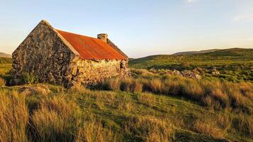 Beautiful landscape scenery with old rusty tin roof cottage on green hill at Connemara National park in County Galway, Ireland photo