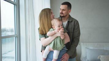 feliz família às lar. mãe pai segurando pequeno criança pequena criança. mãe Papai bebê menina relaxar jogando tendo Diversão junto. mulher homem abraçando abraçando bebê com amor Cuidado. pai do seio alimentando bebê video