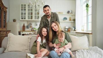 gelukkig familie Bij huis. moeder vader twee kinderen dochters ontspannende Aan sofa binnen. mam vader ouders baby meisjes kinderen kom tot rust spelen hebben pret samen. familie glimlachen lachend genieten van inschrijving moment video