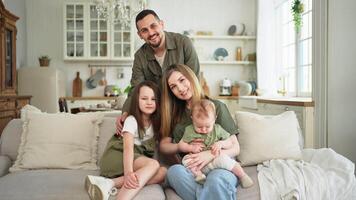 content famille à maison. mère père deux les enfants filles relaxant sur canapé intérieur. maman papa Parents bébé les filles des gamins se détendre en jouant ayant amusement ensemble. famille souriant en riant profiter soumissionner moment video