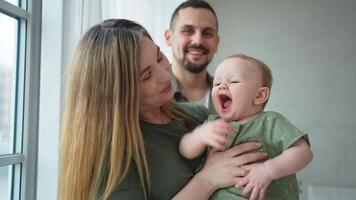 content famille à maison. mère père en portant peu bambin enfant. maman papa bébé fille se détendre en jouant ayant amusement ensemble. femme homme étreindre embrassement bébé avec l'amour se soucier. parent de Sein alimentation bébé video