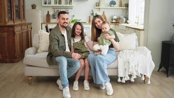 Happy family at home. Mother father two children daughters relaxing on sofa indoor. Mom dad parents baby girls kids relax playing having fun together. Family smiling laughing enjoying tender moment video