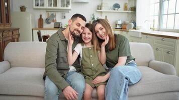 content famille à maison. mère père les enfants fille relaxant sur canapé intérieur. maman papa Parents enfant fille se détendre en jouant étreindre ayant amusement ensemble. famille souriant en riant profiter soumissionner moment video