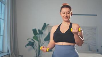 Fitness workout training. Woman picking up dumbbells. Plus size female doing sports exercise at home indoor. Girl in sportswear have workout weight training for weight loss. Sport and fitness video