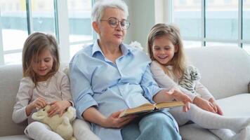 glücklich Familie beim heim. zwei Mädchen Schwestern Zwillinge Oma lesen Geschichte Buch zusammen. gut Zeit beim heim. Oma Lehren Enkelinnen lesen Buch Märchen erzählen Geschichte. Familie Generationen video