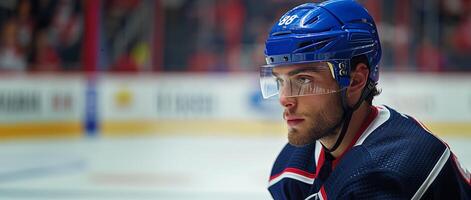 A hockey player in a blue helmet and jersey stands sideways. Hockey arena in the background. Copy space photo